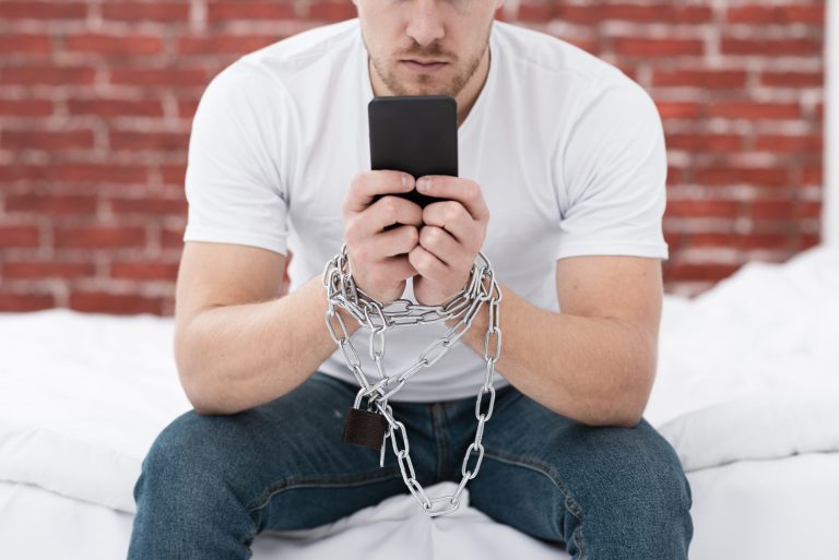 man holding his phone while he is tied up with chains 1